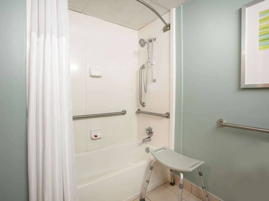 A bathroom with a shower, grab bars, a white bathtub, and a wheelchair-accessible bench.