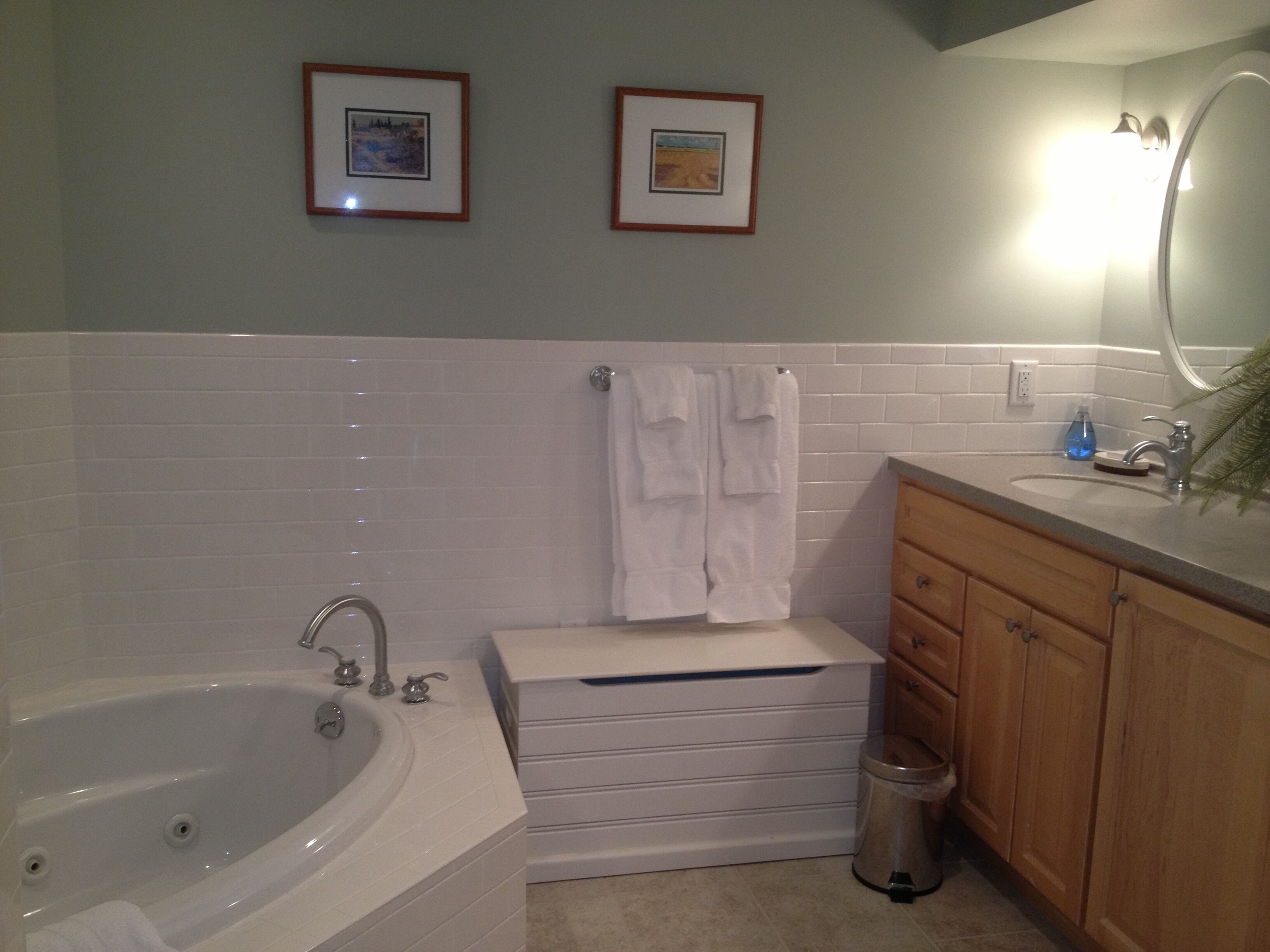 A bathroom with a bathtub, a sink, a mirror, and a toilet. There are two framed pictures on the wall.