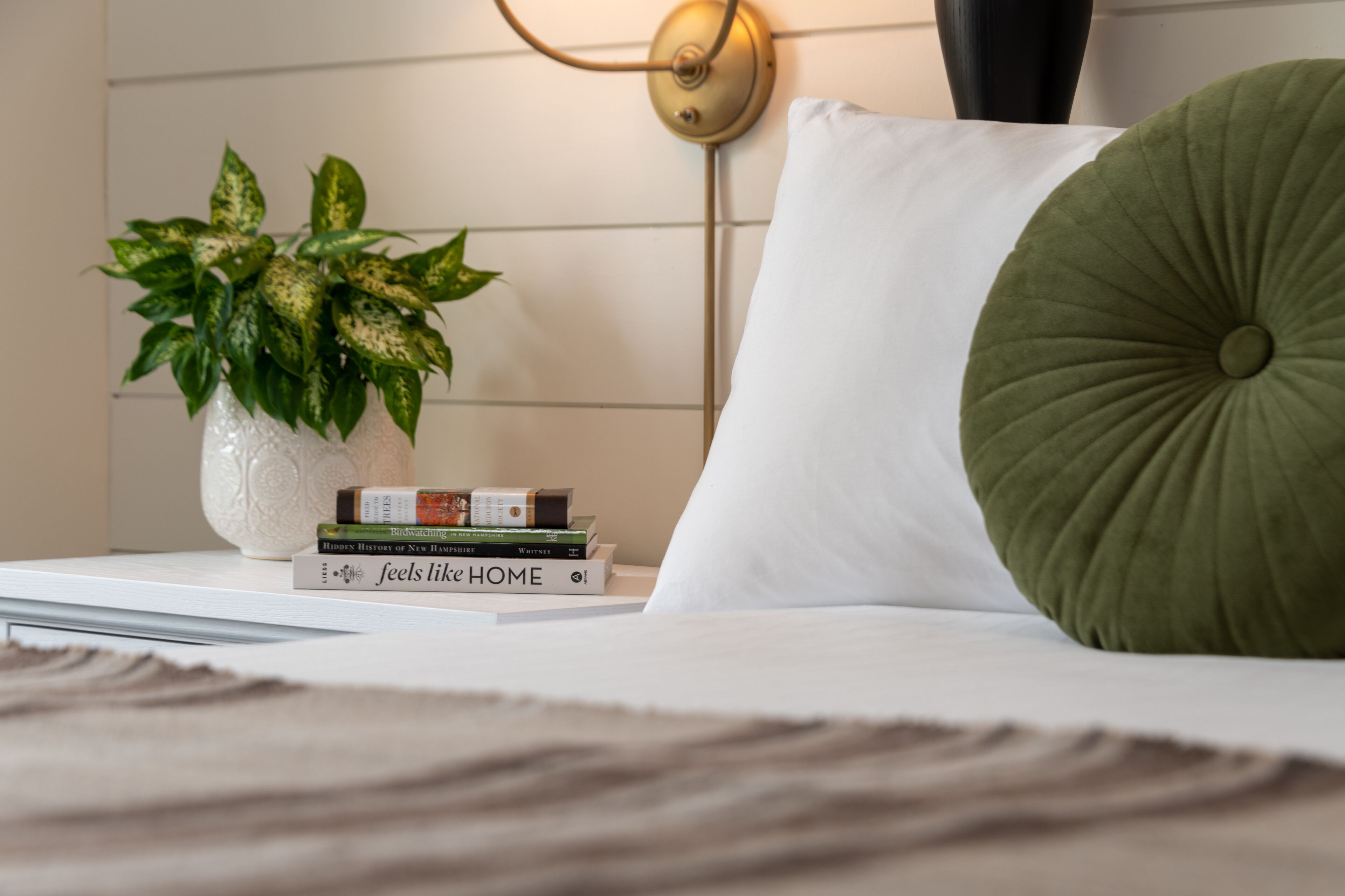 A neatly arranged bedroom with a bedside table holding a potted plant and a stack of books.
