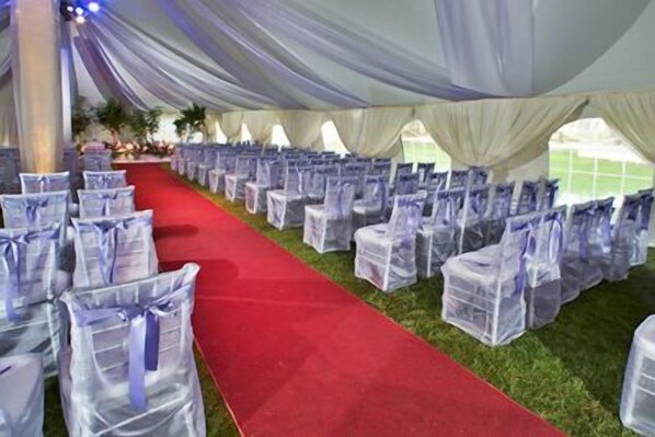 A tented event space with rows of chairs covered in plastic, a red carpet aisle, and draped fabric overhead.