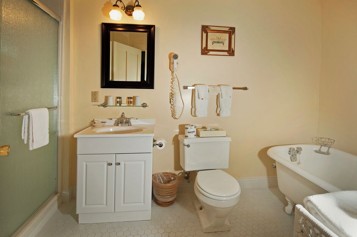A bathroom with a white sink, toilet, and clawfoot bathtub. There is a mirror above the sink, a towel rack with towels, and a framed picture on the wall.