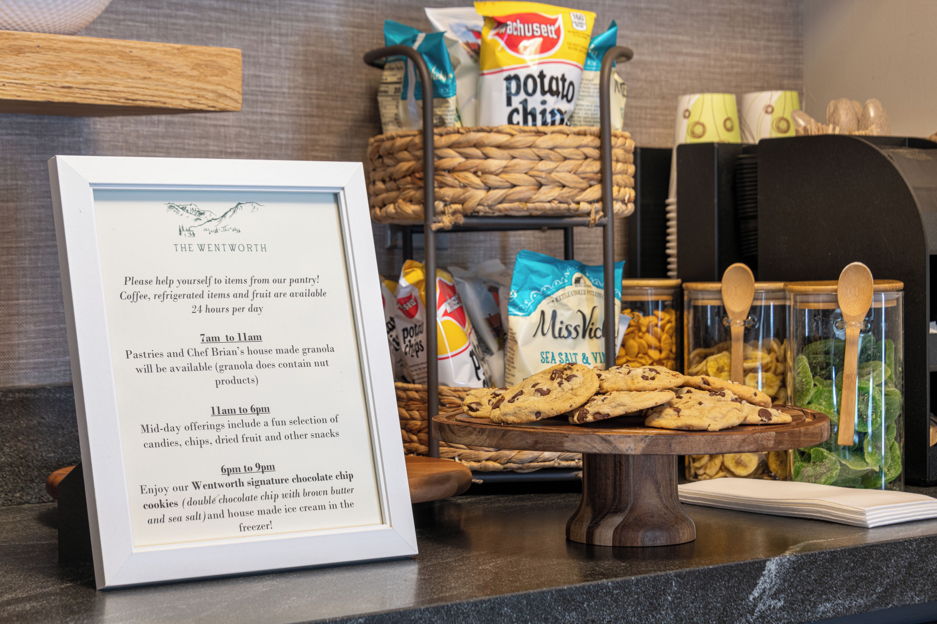 Un tableau affichant le menu, avec un menu encadré, un panier de biscuits et une sélection de collations et de chips.