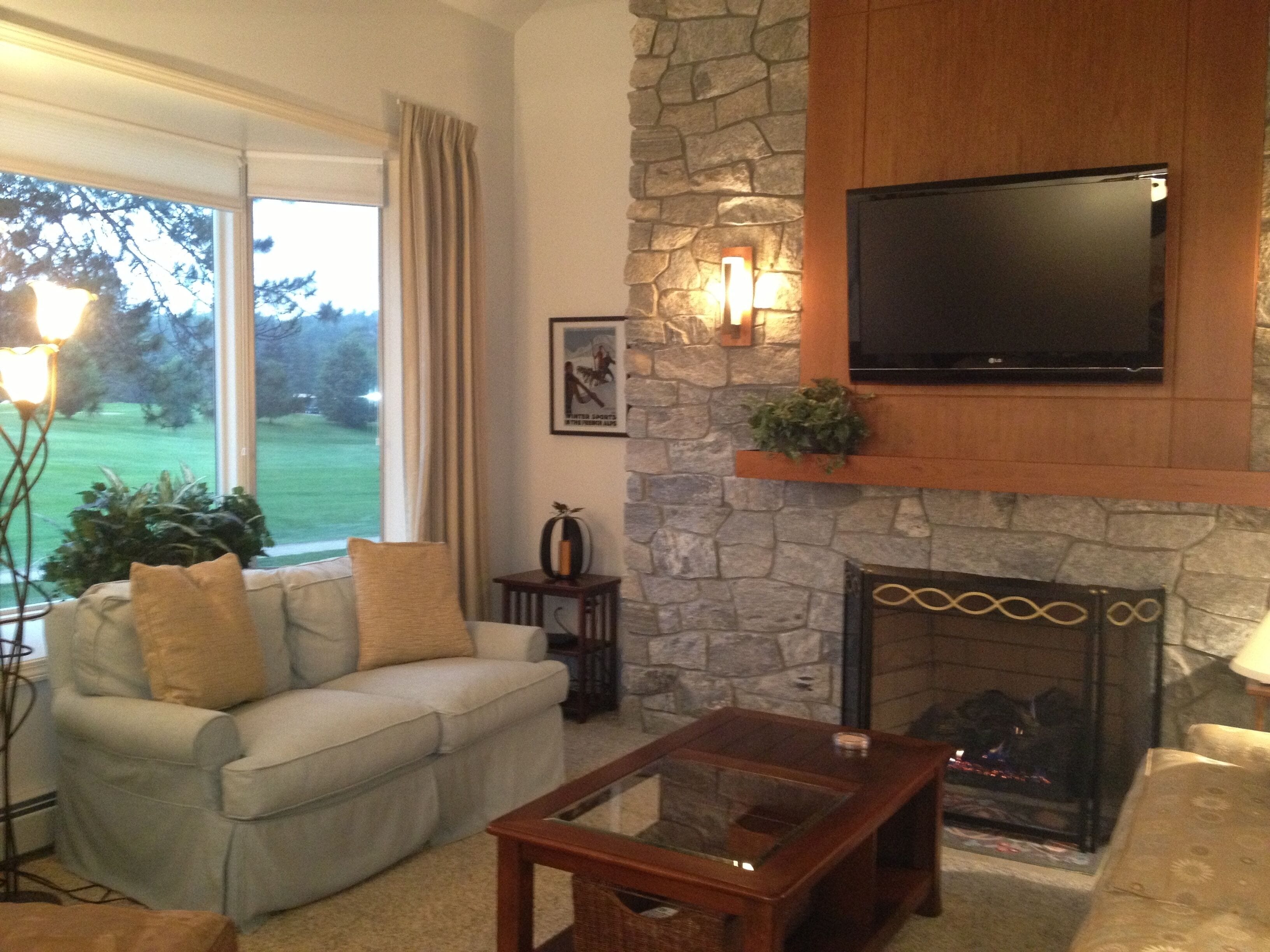 A living room with a stone fireplace, a flat-screen TV mounted above it, a sofa with cushions, and a coffee table.