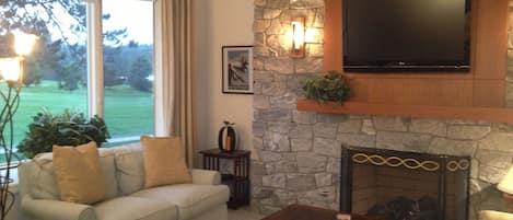 A living room with a stone fireplace, a flat-screen TV mounted above it, a sofa with cushions, and a coffee table.