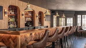 A bar area with a wooden herringbone floor, leather bar stools, and a long bar counter. - The Wentworth (Jackson)