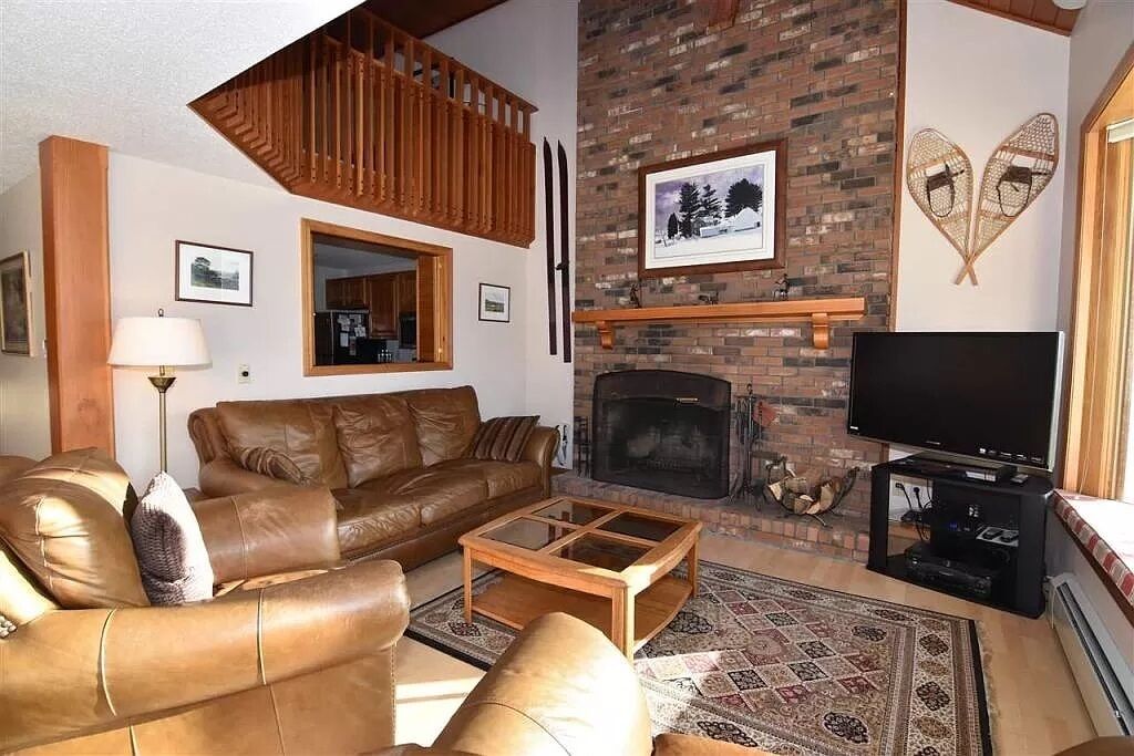 A living room with a fireplace, leather sofas, a TV, and a wooden staircase.