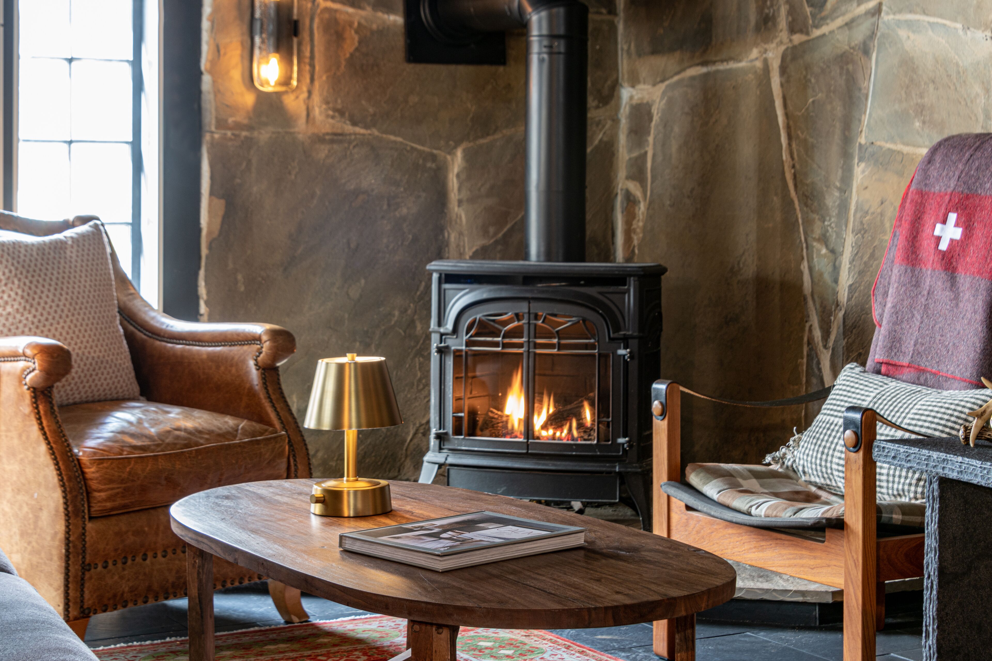 A cozy room with a stone wall, a fireplace, leather armchairs, a wooden coffee table, and a Swiss flag towel.