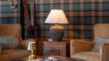 Un ambiente acogedor con dos sillones de cuero, una mesa redonda de madera con un libro y una lámpara, y una pared con estampado de cuadros.
