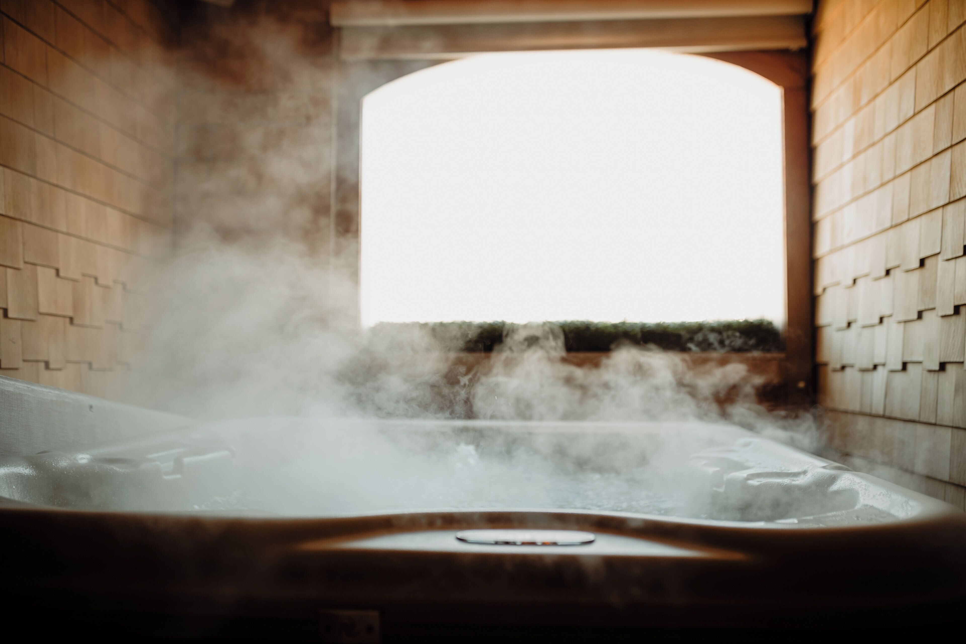 A hot tub with steam rising from the water, surrounded by wooden walls and a window in the background.