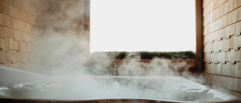 A hot tub with steam rising from the water, surrounded by wooden walls and a window in the background.
