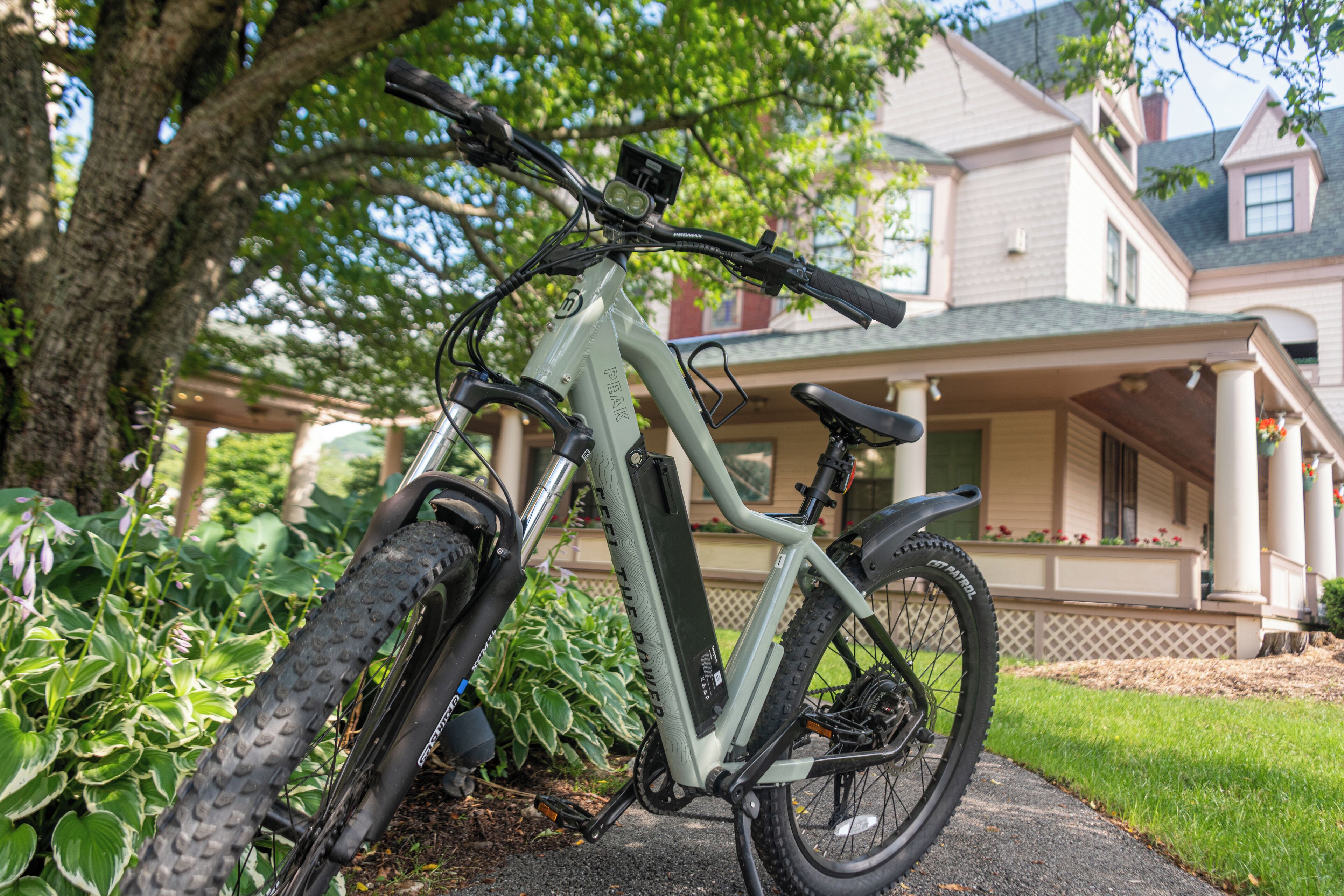 A mountain bike parked in front of a house with a porch and a large tree.