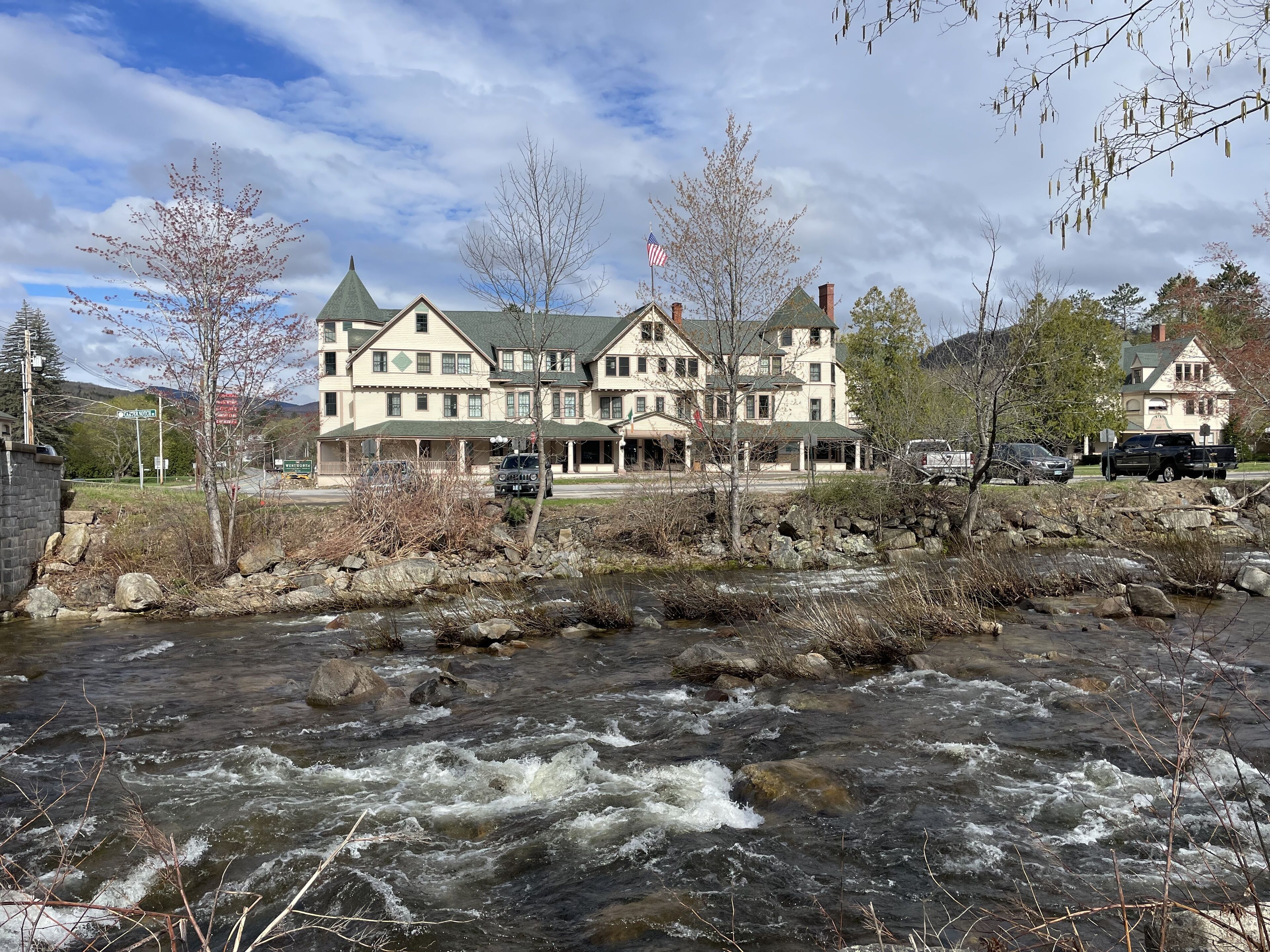 A large, multi-story building with a prominent American flag, situated beside a flowing river with visible rapids.