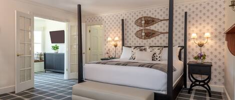 A bedroom with a four-poster bed, a bench, a nightstand with lamps, and patterned wallpaper.