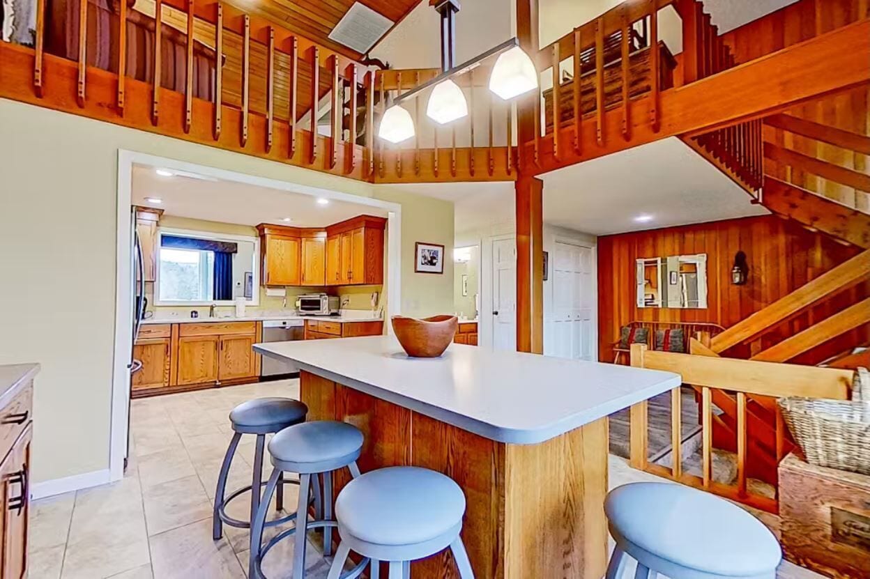 A spacious kitchen with a central island, wooden staircase, and a cozy seating area.