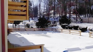 A snow-covered outdoor area with a wooden fence, a bench, and a view of trees and a building in the background. - Iron Horse Inn (Simsbury)