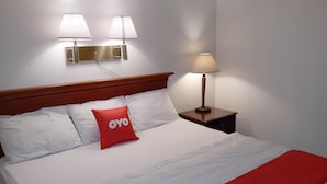A neatly made bed with white bedding and a red pillow, a wooden headboard, and two wall-mounted lamps. - Iron Horse Inn (Simsbury)