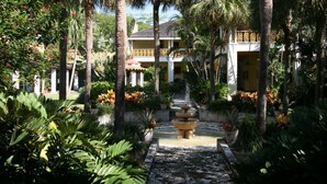 A courtyard with a fountain, palm trees, and a building with balconies. - Great Escape Apartments by Lowkl (Lauderdale-by-the-Sea)
