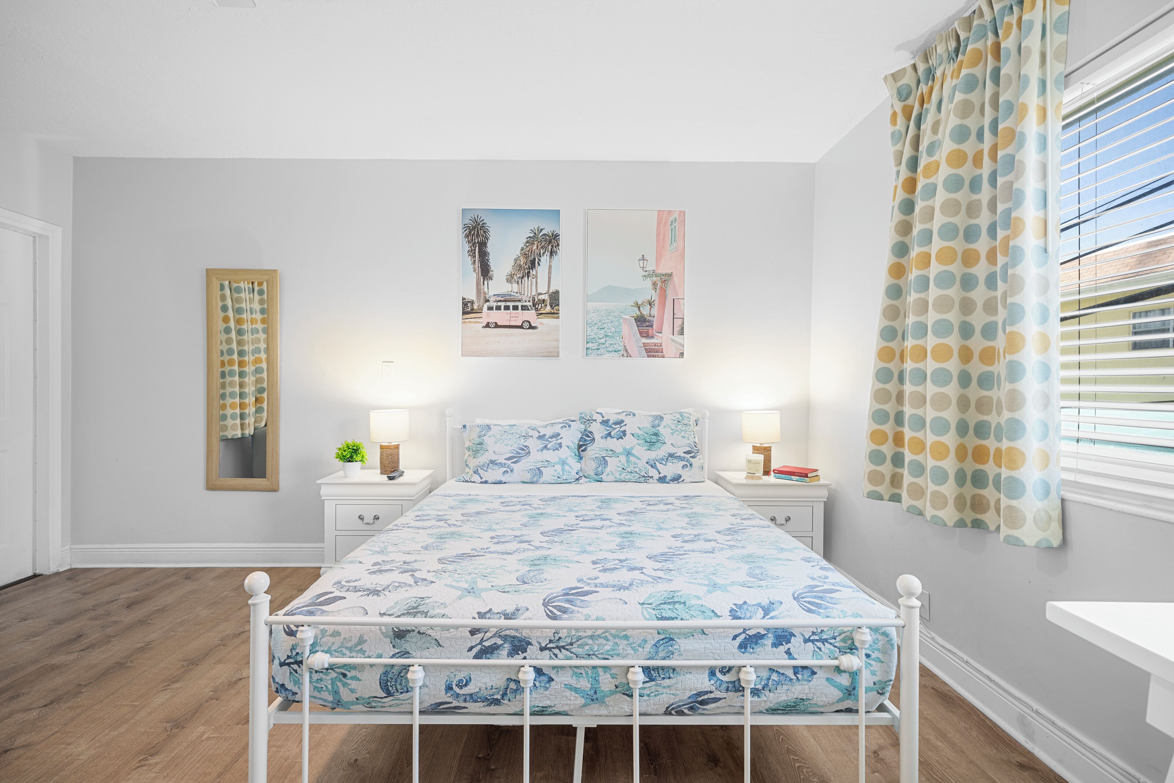 A bedroom with a bed, two bedside tables, a nightstand, a mirror, and a window with curtains.