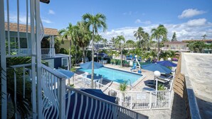 A pool area with palm trees, lounge chairs, and umbrellas. - Great Escape Apartments by Lowkl (Lauderdale-by-the-Sea)