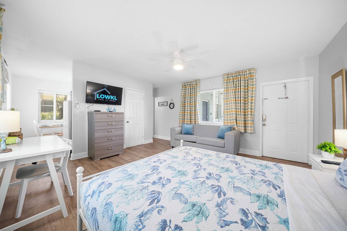 A bedroom with a bed, a TV, a dresser, a window with curtains, and a ceiling fan.