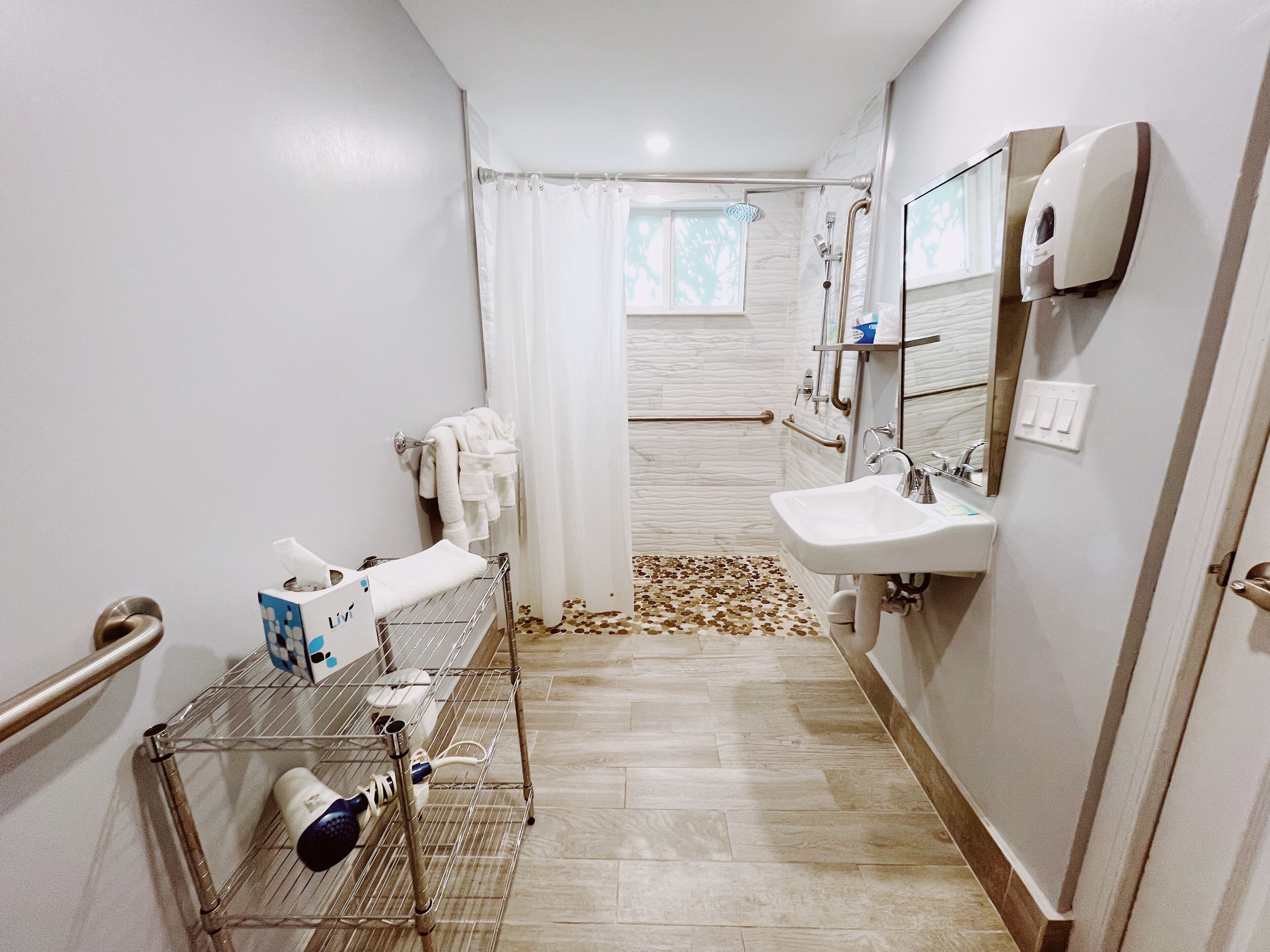 A bathroom with a shower, a sink, a hand dryer, and a towel rack.