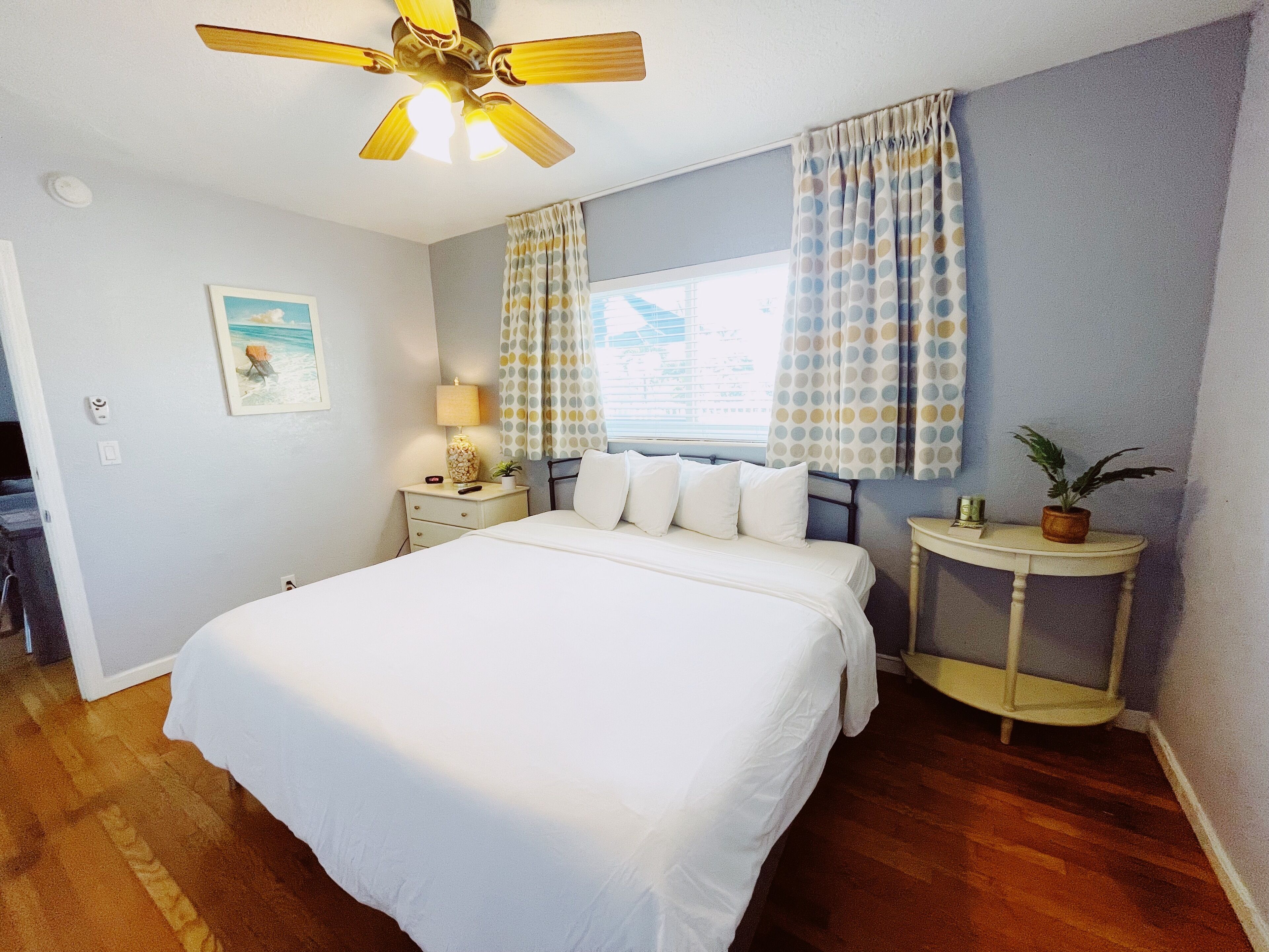 A hotel room with a bed, a nightstand with a lamp, a ceiling fan, and a window with curtains.