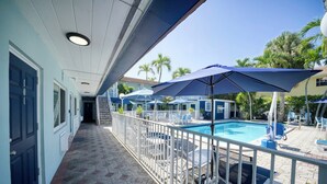 A pool area with a covered walkway, lounge chairs, and umbrellas. - Great Escape Apartments by Lowkl (Lauderdale-by-the-Sea)