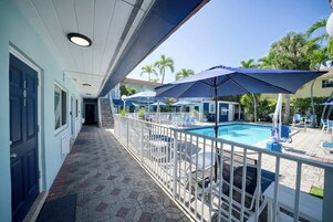 A pool area with a covered walkway, lounge chairs, and umbrellas.