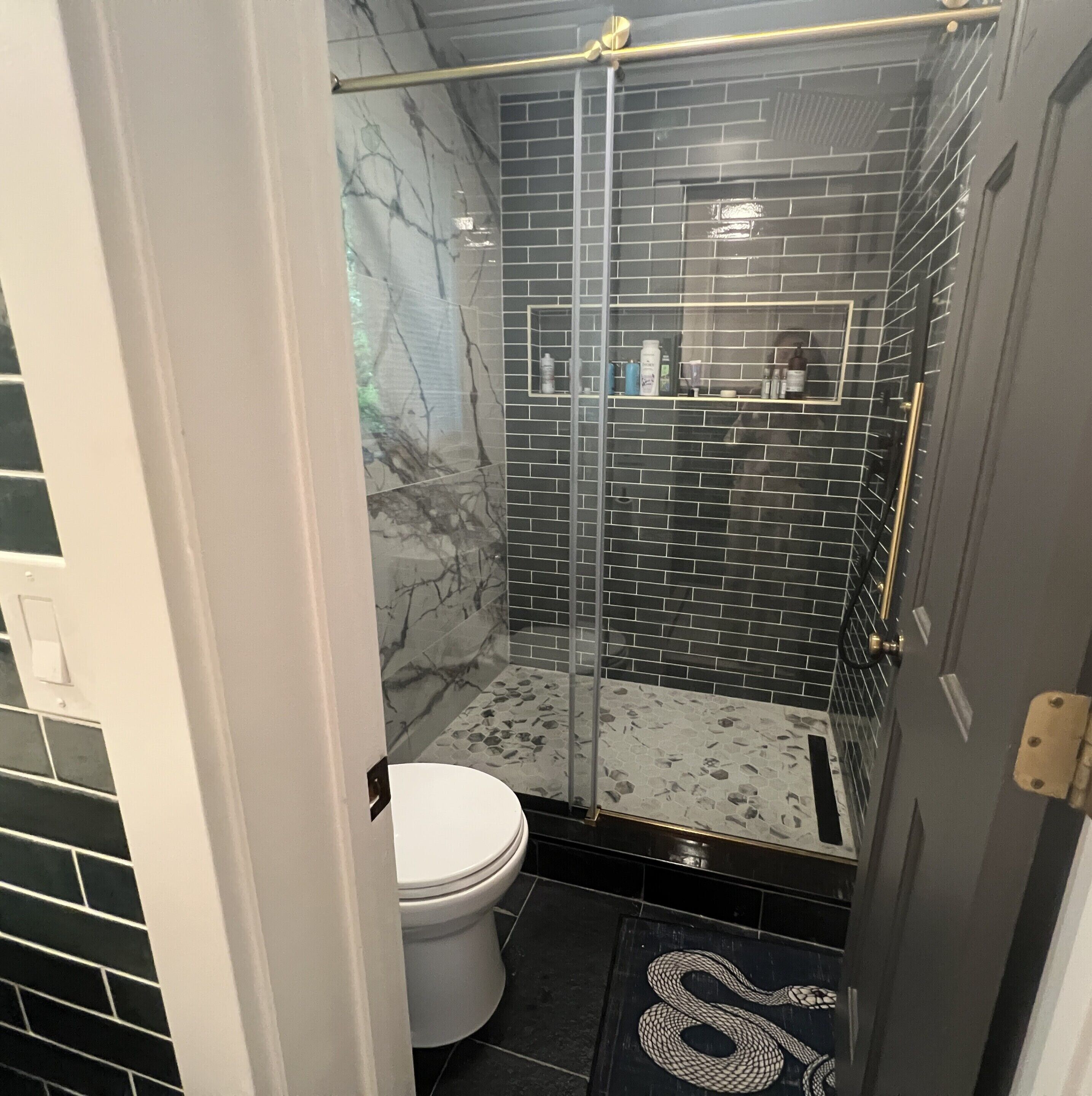 A bathroom with a glass shower enclosure, a white toilet, and a tiled floor.