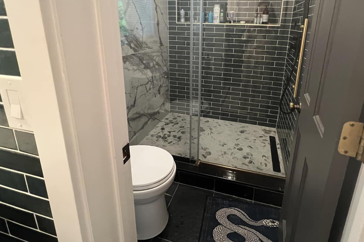 A bathroom with a glass shower enclosure, a white toilet, and a tiled floor.