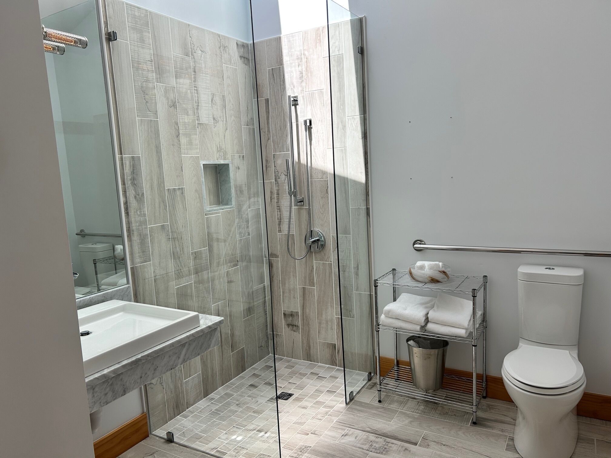 A modern bathroom with a glass-enclosed shower, a marble sink, and a toilet with a towel rack.