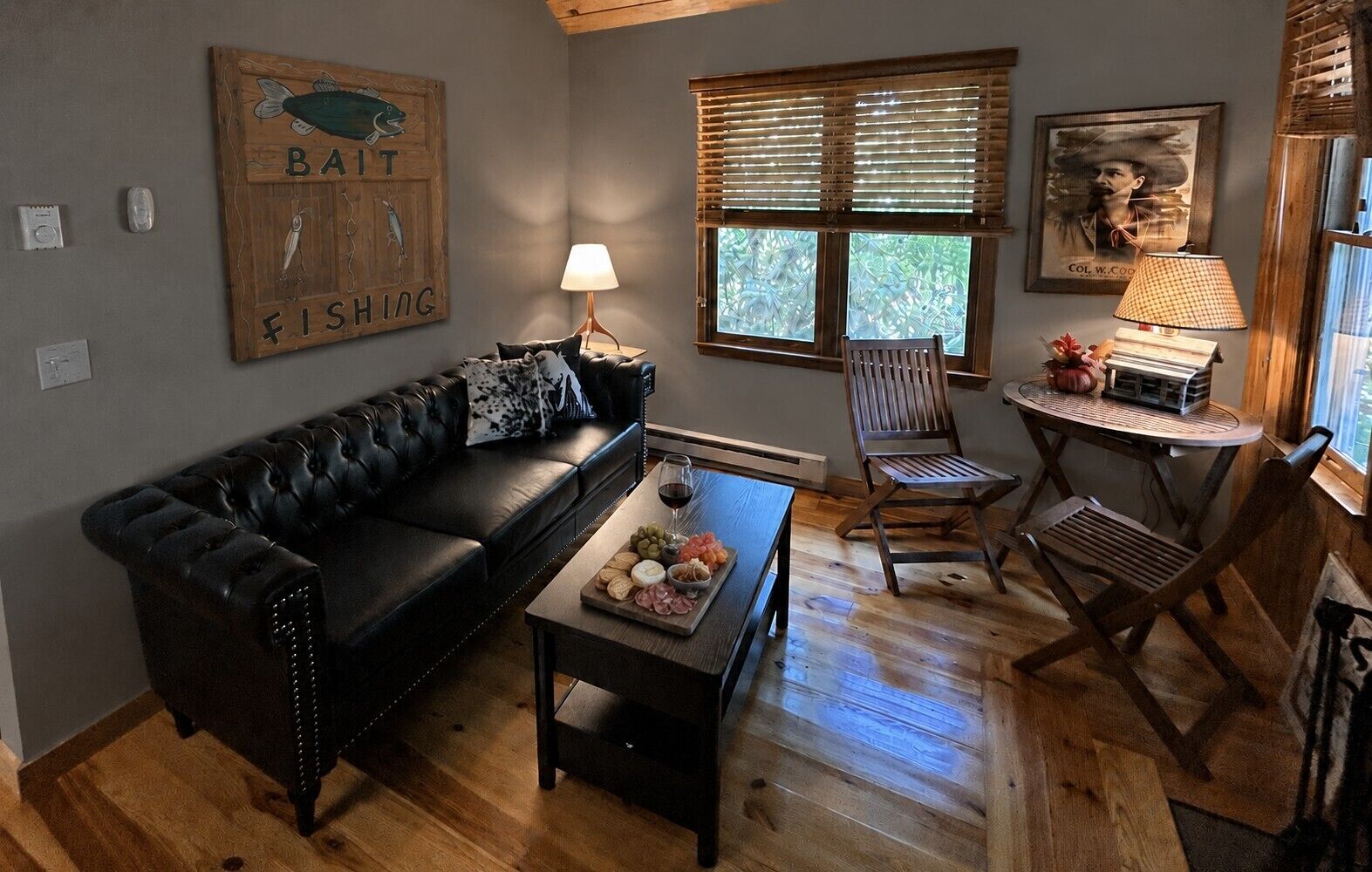 A cozy living room with a black leather sofa, a wooden coffee table with snacks, a lamp, and a window with blinds.