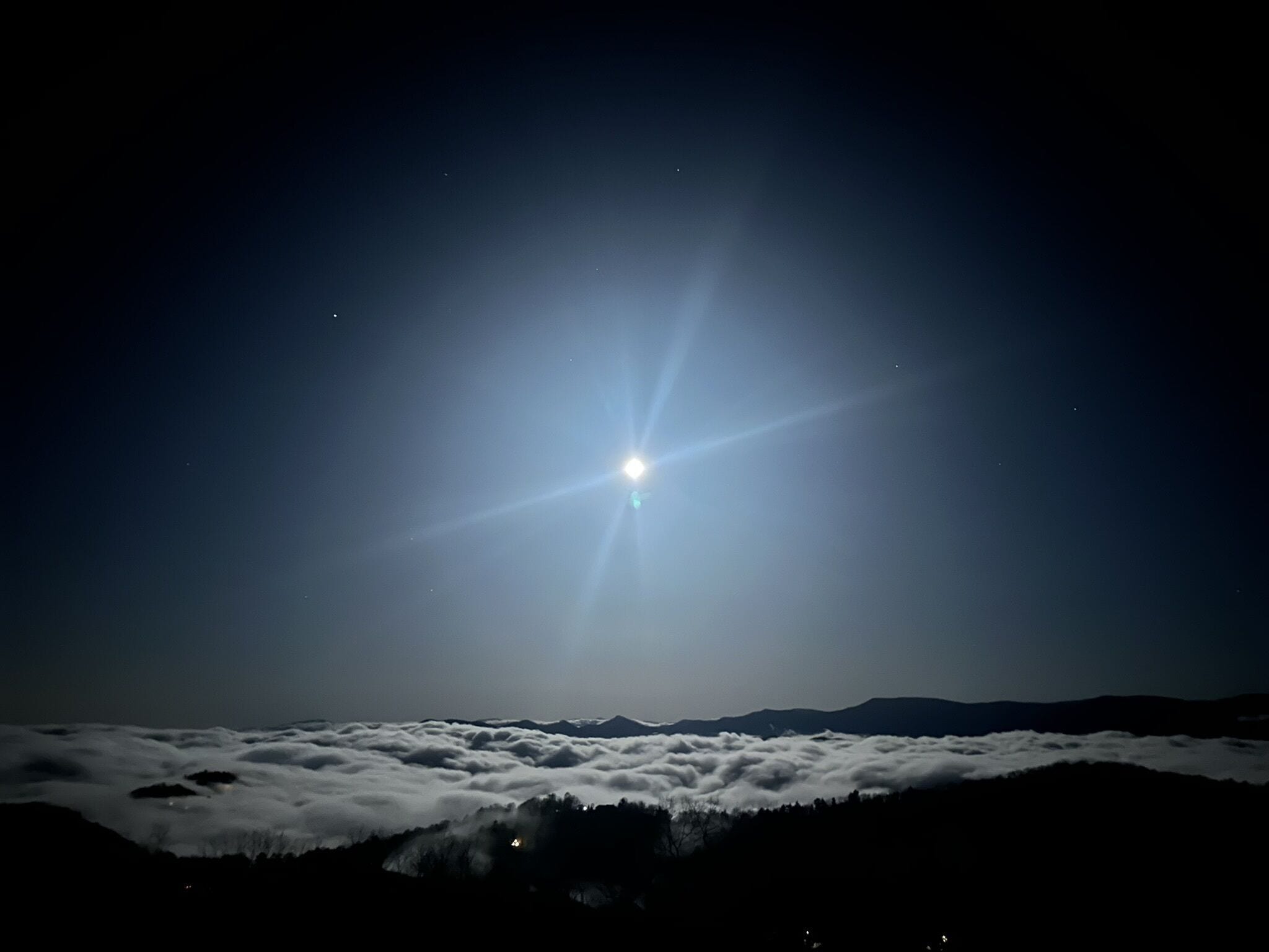 A night sky with a bright star or planet, clouds below, and a mountain range in the distance.