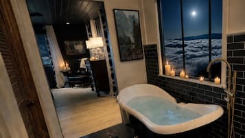 A modern bathroom with a freestanding bathtub, a window with a night view, and a dark floor.