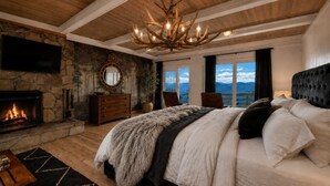 Una camera da letto con camino in pietra, un letto grande, un lampadario e vista sulle montagne.