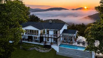 A modern house with a pool, surrounded by lush greenery and a scenic mountain backdrop.