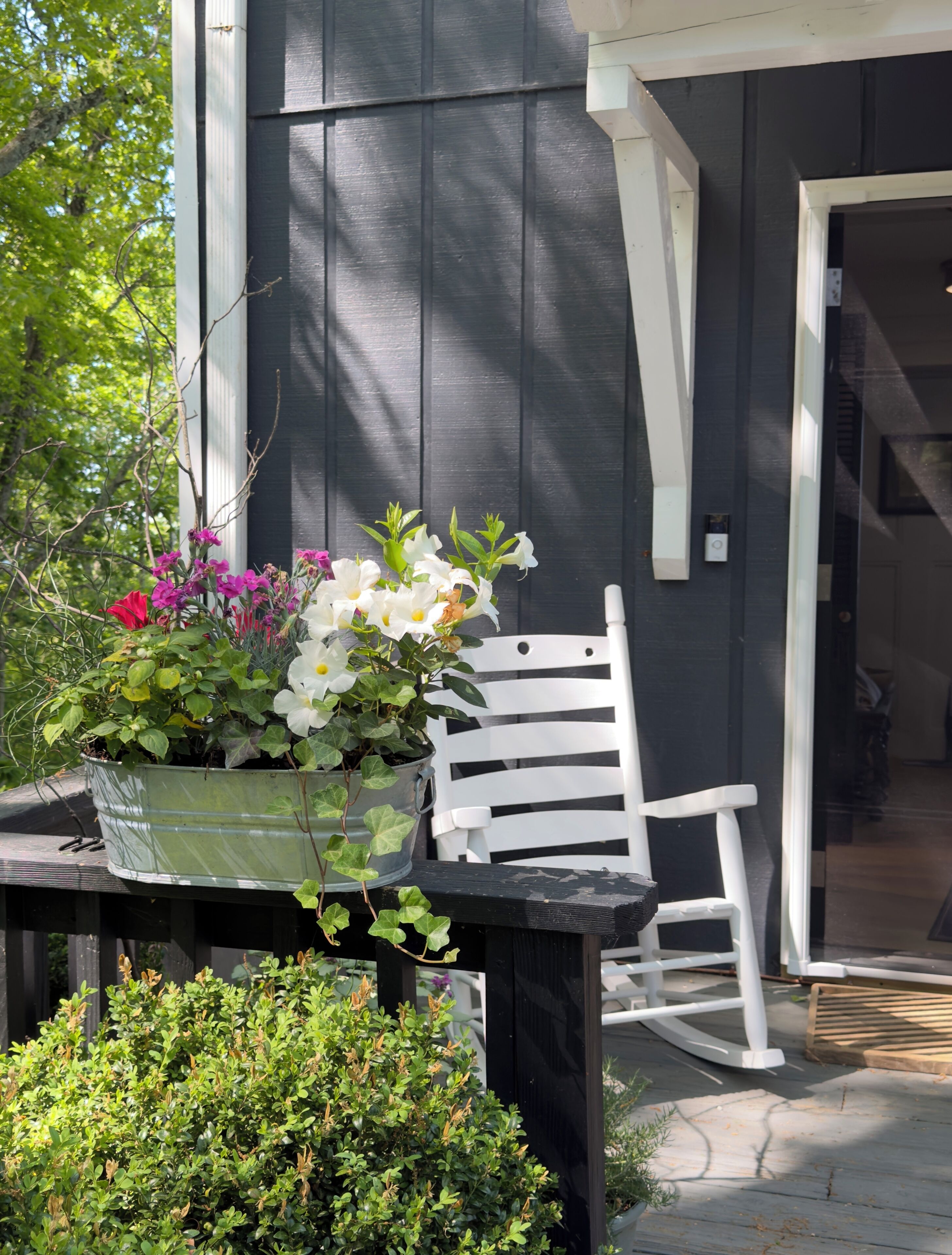 A black exterior wall with a white door and a white rocking chair.