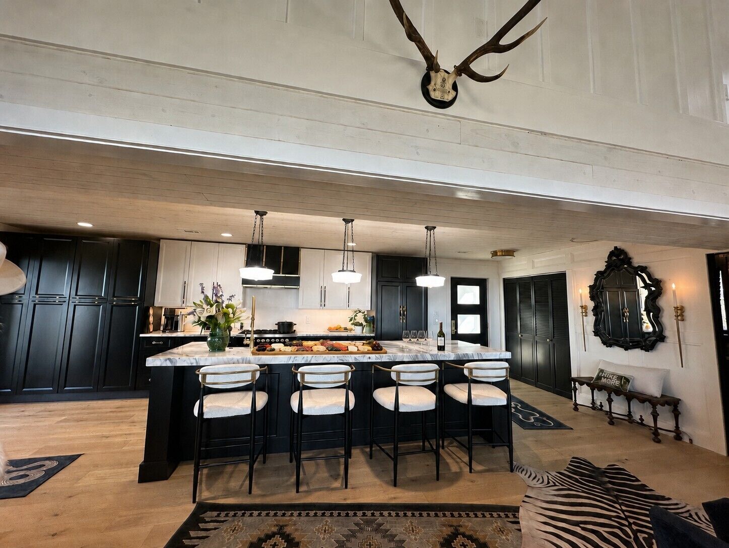 A modern kitchen with a large island, dark cabinetry, pendant lighting, and a mounted antler.