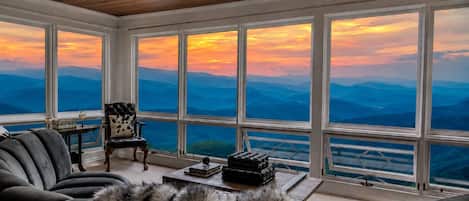 A room with a large window, a leather sofa, a chair, and a fur throw.
