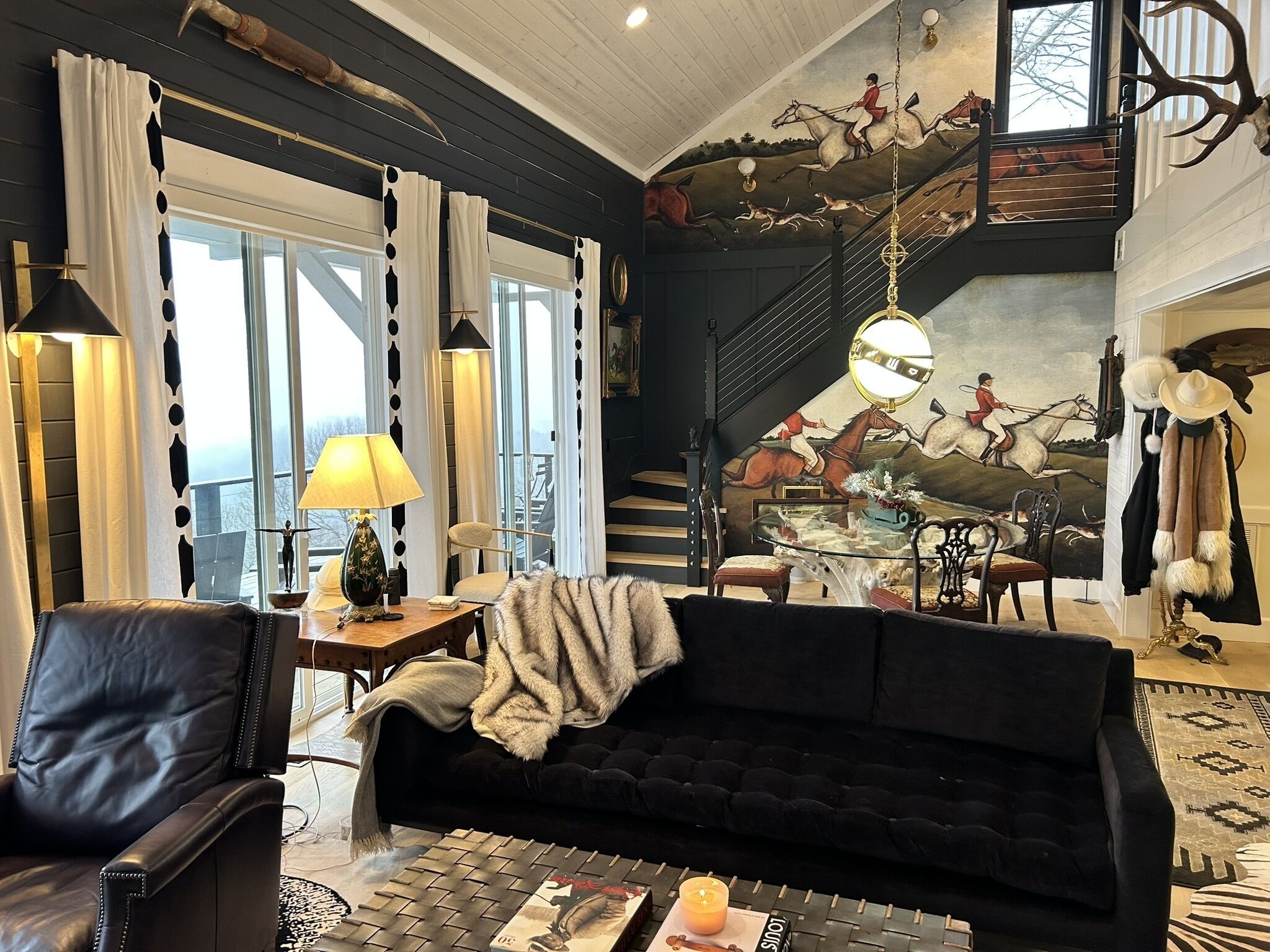 A living room with a black sofa, a coffee table, a fireplace, and a staircase with a mural.
