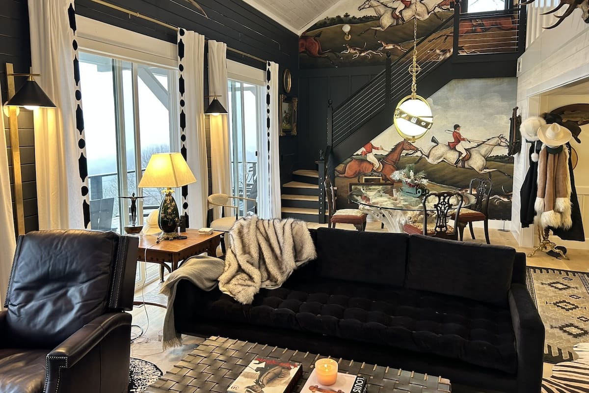 A living room with a black sofa, a coffee table, a fireplace, and a staircase with a mural.