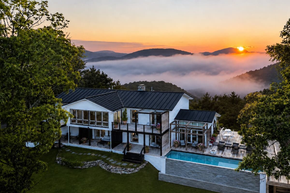 A modern house with a pool, surrounded by lush greenery and a view of mountains at sunset.