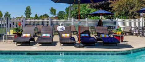 A poolside area with lounge chairs and umbrellas, a white picket fence, and a clear blue pool.