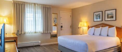 A hotel room with a large bed, two bedside lamps, a desk with a lamp, a window with curtains, and a door.