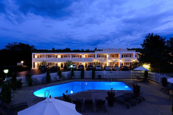A hotel with a swimming pool, outdoor seating, and a white fence surrounding the area.