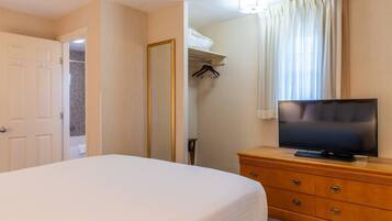 Habitación de hotel con cama, cómoda de madera, televisor, armario y baño visible a través de una puerta abierta.
