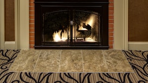 A fireplace with a fire, a framed picture above it, and wall sconces on either side. - Port Inn and Suites Portsmouth, an Ascend Collection Hotel (Portsmouth)