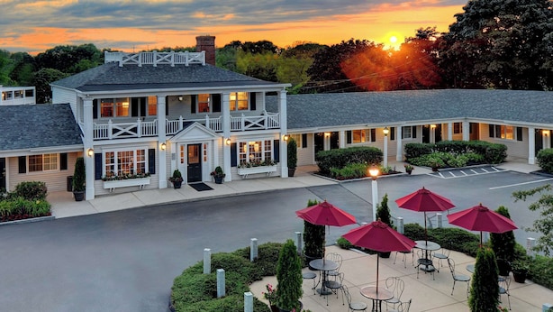 A two-story building with a balcony, outdoor seating area with red umbrellas, and a parking lot. - Port Inn and Suites Portsmouth, an Ascend Collection Hotel (Portsmouth)