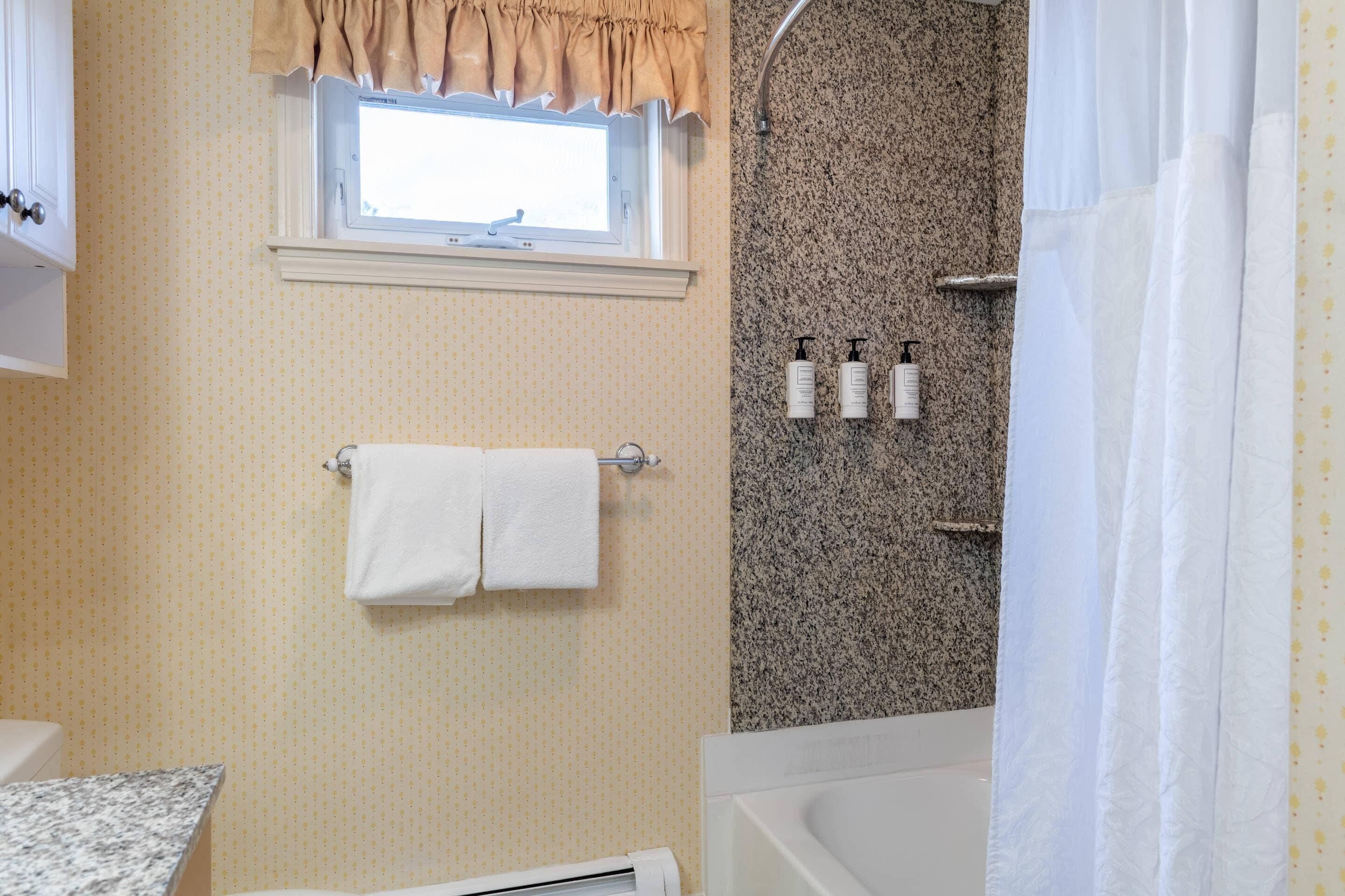 Une salle de bain avec une fenêtre, un porte-serviettes, une douche avec un mur en granit et une baignoire.
