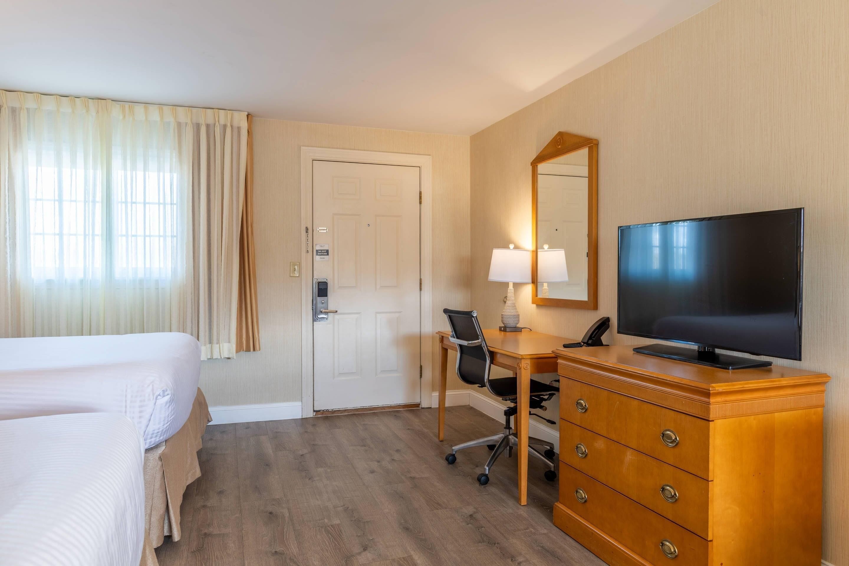 A hotel room with two beds, a desk with a chair, a television, and a dresser.